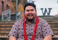 Nestor wearing a red and black button-down shirt and a red lei, sitting on the steps of a UW campus
