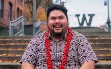 Nestor wearing a red and black button-down shirt and a red lei, sitting on the steps of a UW campus