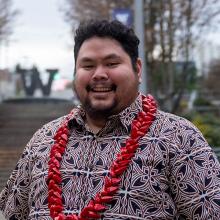 Nestor wearing a red and black patterned shirt with a red lei