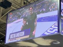 Photo taken of the jumbotron showing JP with his son on the basketball court smiling and the crowd looking on