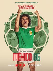 A Mexican football player wearing a green shirt and white shorts stands in front of a large football with both of his fists pumped in the air