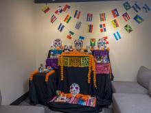 An ofrenda sits in the corner of the La Plaza room, adorned with photos, candles, and marigolds in honor of loved ones