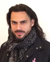 JP Anderson wearing an interwoven scarf and black coat stares forward at the camera