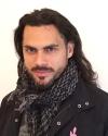 JP Anderson wearing an interwoven scarf and black coat stares forward at the camera