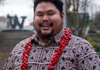 Nestor wearing a red and black patterned shirt with a red lei