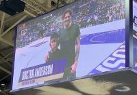 Photo taken of the jumbotron showing JP with his son on the basketball court smiling and the crowd looking on