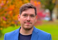 Juan Llamas-Rodriguez faces the camera wearing a dark navy blue shirt with a light blue blazer