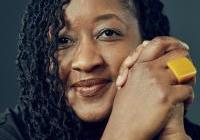 A headshot photo of LaShawnDa smiling with her hands clasped together in front of a dark gray background