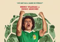 A Mexican football player wearing a green shirt and white shorts stands in front of a large football with both of his fists pumped in the air