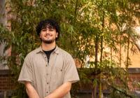 Udall Scholar Lorenzo McCleese Lorenzo McCleese smiles while standing in front of a bamboo tree wearing a light tan striped button down with a black undershirt