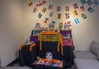 An ofrenda sits in the corner of the La Plaza room, adorned with photos, candles, and marigolds in honor of loved ones