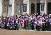 Former UW students from the Long Journey Home Ceremony stand on the steps of Suzzallo and Allen Libraries in graduation attire